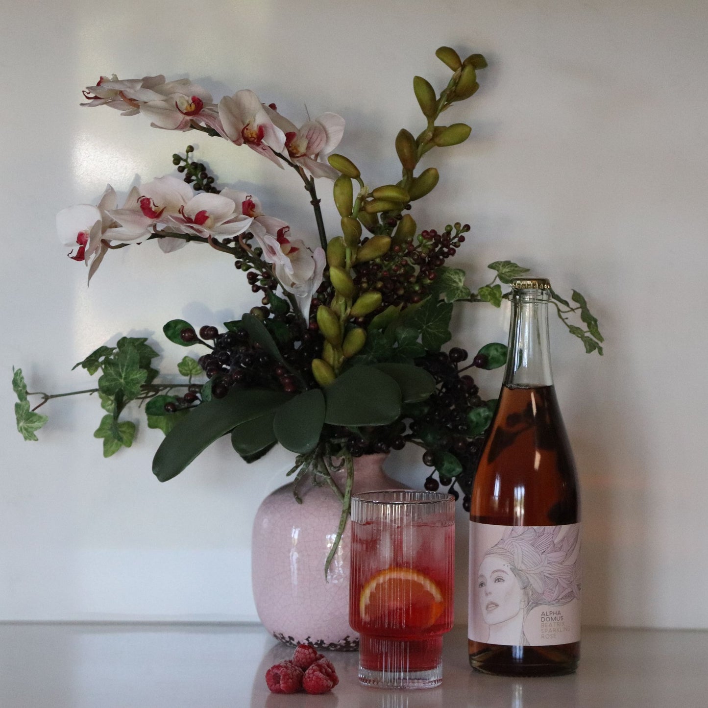Orchids and berries pot in setting with a bottle of rose , a glass and raspberries